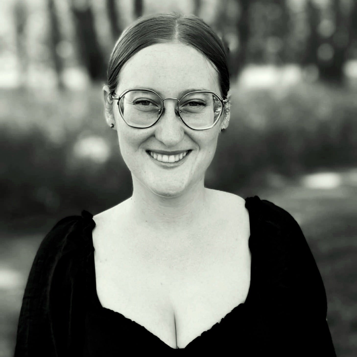 Black and white photo of a person wearing glasses and a black top outdoors.