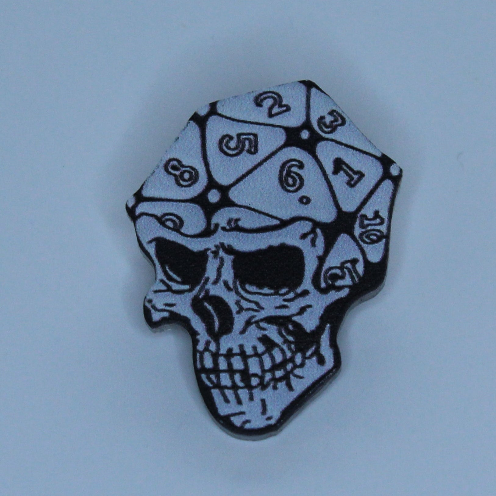 A small skull-shaped acrylic pin with a black and white patterned bandana, centered on a solid light blue background.