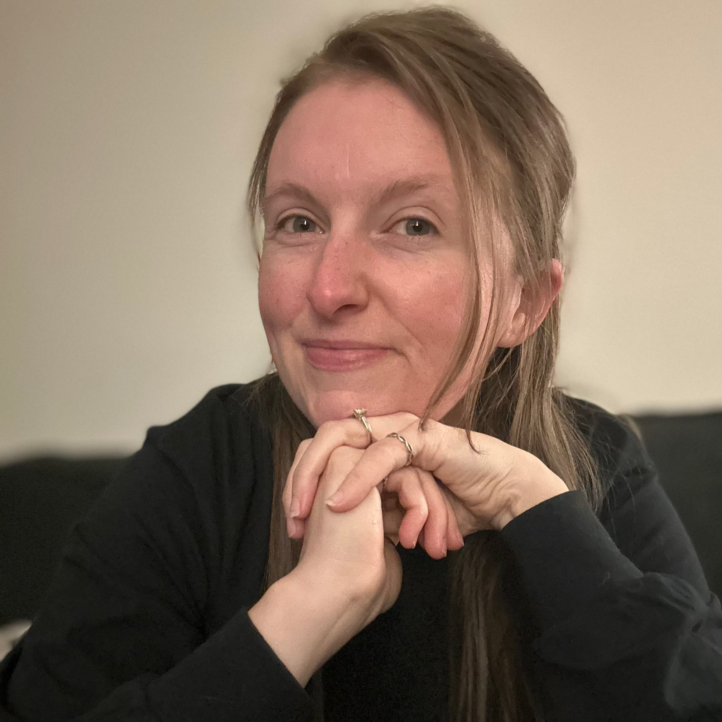 Woman with hands clasped together in front of a neutral background