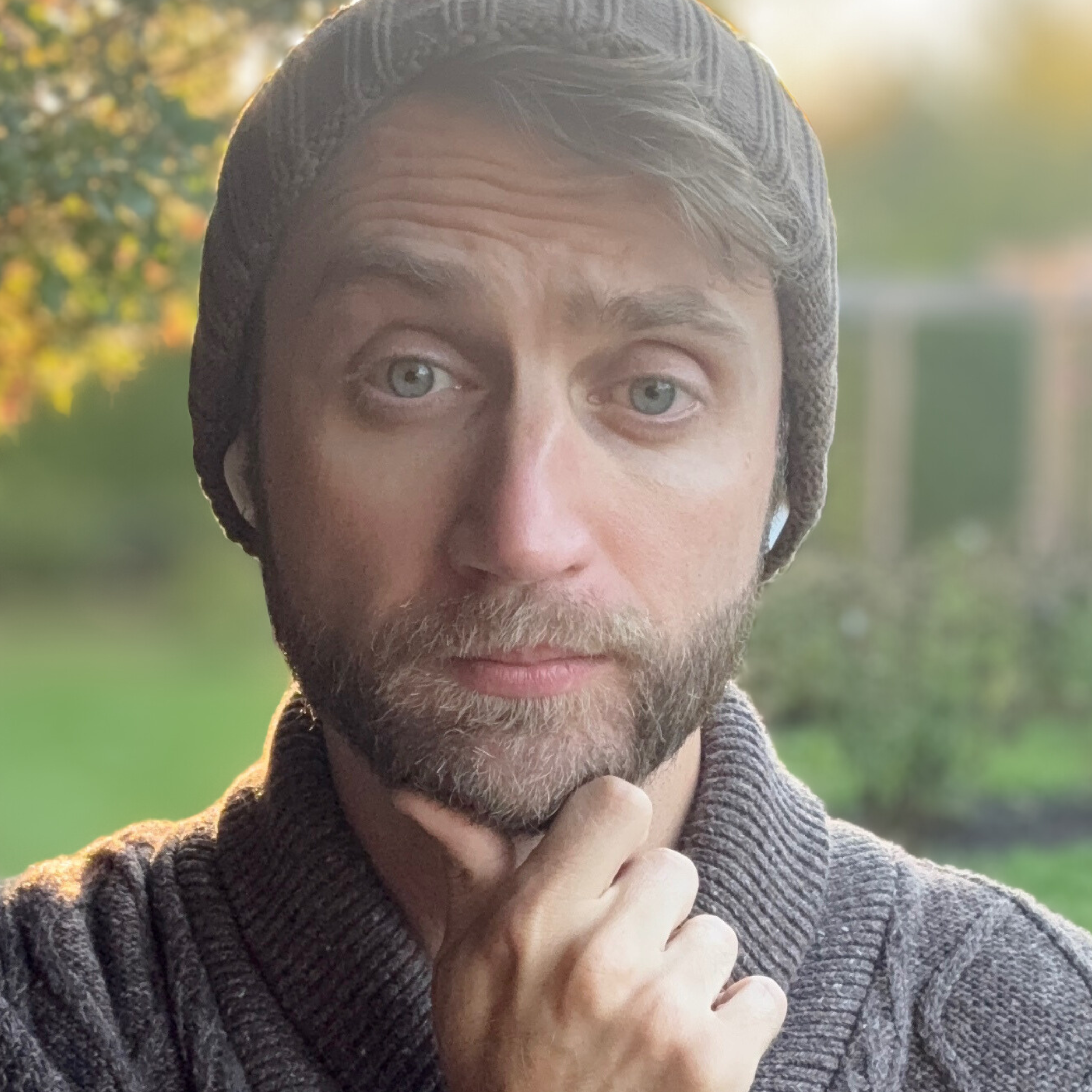 Man wearing a gray knit hat and sweater with a blurred outdoor background