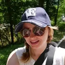 Person wearing a cap and sunglasses outdoors with greenery in the background