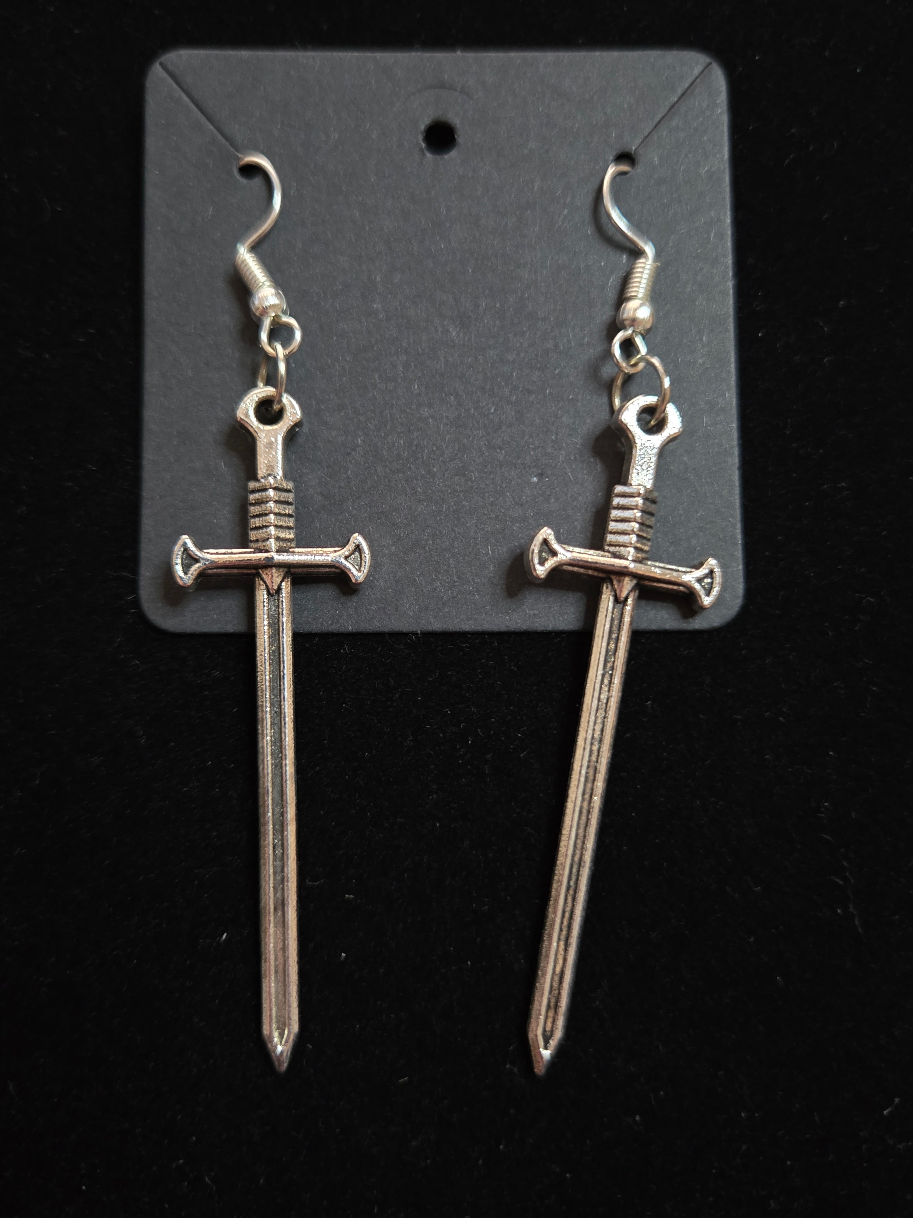 Silver sword-shaped earrings on a black card against a black background