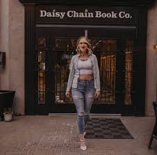 Woman standing in front of a store named 'Daisy Chain Book Co.'