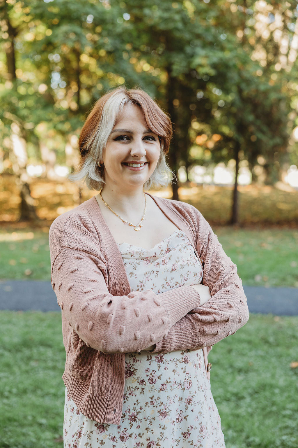 Woman wearing a pink cardigan over a floral dress in a park setting