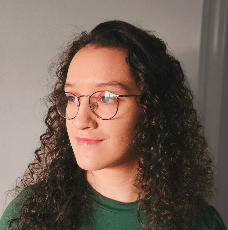 Person with curly hair wearing glasses and a green shirt against a plain background
