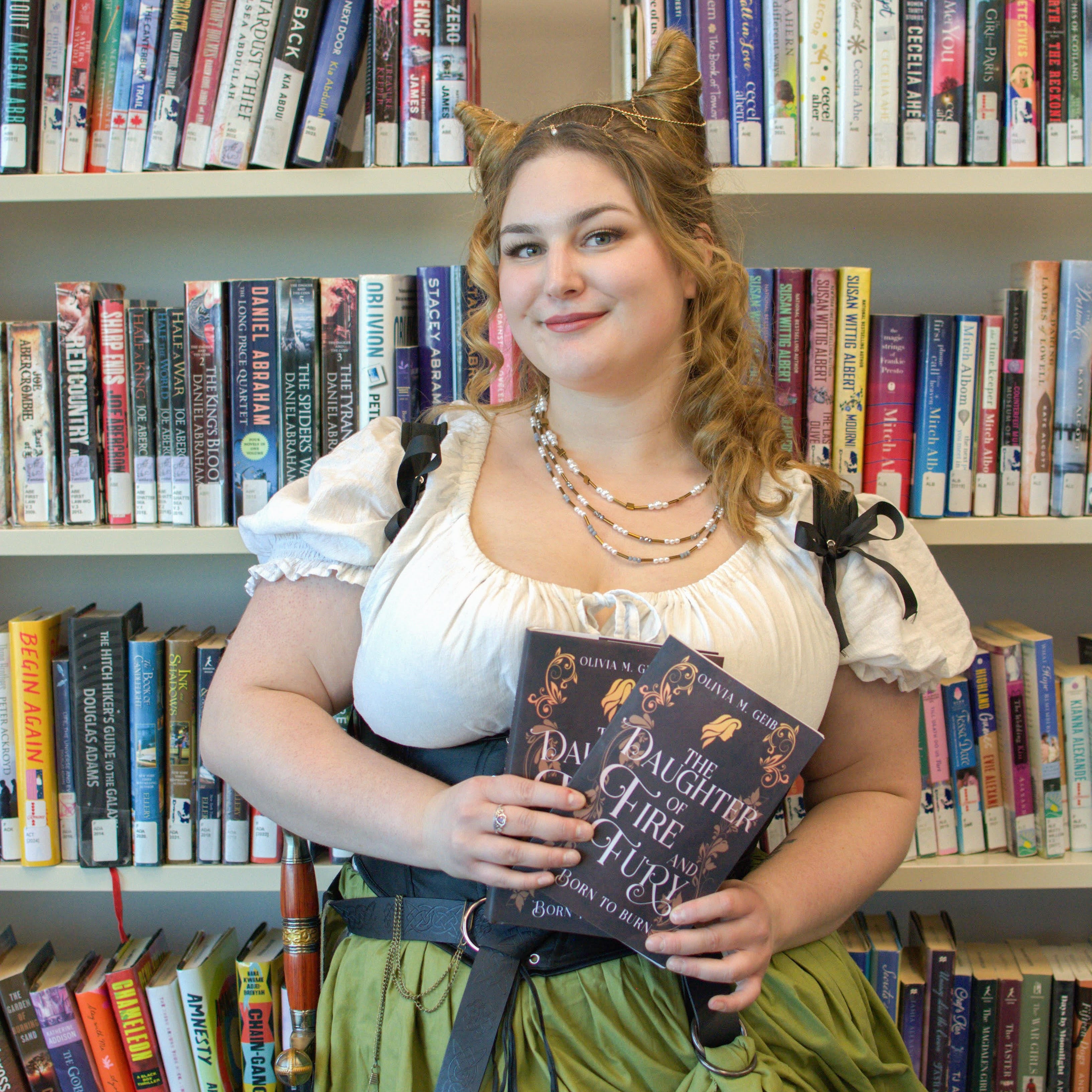Person in a costume holding a book in front of a bookshelf